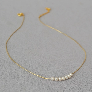 Detail of 7 round white pearls on a thin gold-plated chain minimalist necklace
