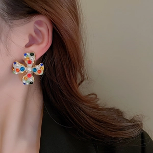Close-up of gold cross earring with multi-color stones and pearls on model ear