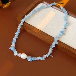 Detailed shot of aquamarine stones and white pearl necklace on a rustic wooden tray
