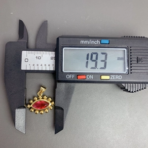 Macro shot of gold evil eye pendant with red zircon measuring 19.3mm on digital caliper