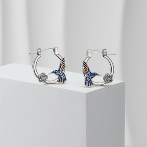 Macro detail of silver hummingbird hoop earrings with colorful enamel floral accents