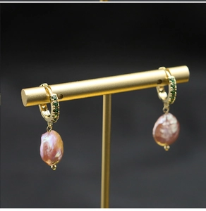 Macro detail of Baroque pearl earring with emerald accents on gold display stand