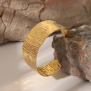 Détail du large bracelet ouvert doré avec une texture ondulée martelée sur pierre