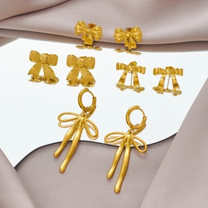Elegant gold bow earrings collection on mirror surface with satin background