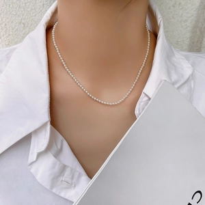 Close-up of minimalist 2mm white pearl choker necklace worn with a white blouse