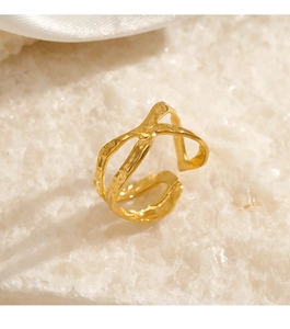 Close-up of golden crossover ring with hammered texture on a white stone surface