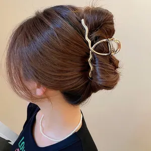 Minimalist golden wavy metal hair claw clip shown on model hair from side-back view