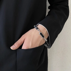 Detail of a men's obsidian bracelet with silver chain on a model wearing a suit