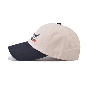 Detail of red cherry embroidery and calligraphy text on a beige cotton baseball cap