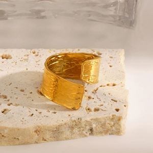 Golden wide open ring with hammered texture displayed on a natural travertine stone stand