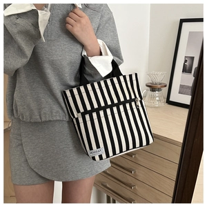 Close-up of black and white striped canvas tote bag with front zipper and fashion label
