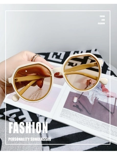 Detail of cream polygon sunglasses held by hand over vintage patterned fabric