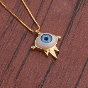 Detail of gold evil eye pendant with blue oil drip and box chain on brown texture