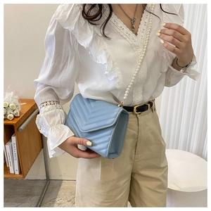 Model wearing a light blue crossbody bag with V-quilted texture and pearl chain strap