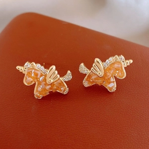 Golden unicorn stud earrings with amber crystals and white zircons on red leather