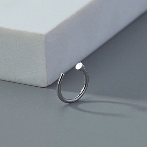 Detailed macro shot of silver C-shaped non-pierced nose ring on minimalist stone base