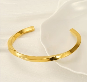 Detailed view of a gold-plated twisted C-shaped bangle on a white ceramic tray