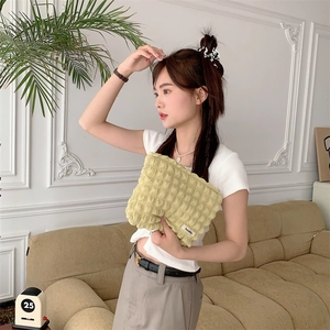 Close-up of yellow bubble textured makeup bag held by a model in a cozy setting