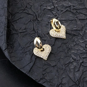 Eleganti orecchini a cuore dorati con pavé di zirconi su sfondo nero strutturato