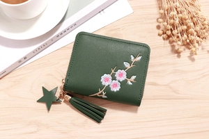 Flat lay of dark green zippered wallet with floral embroidery and tassel on wood table