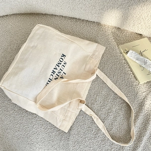 Top-down view of cream canvas tote bag with black lettering on textured fabric