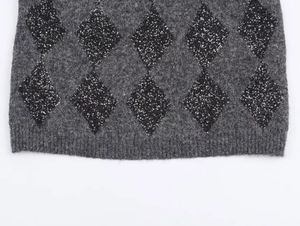 Detailed view of grey knit fabric with black sequin diamond patterns and ribbed hemline