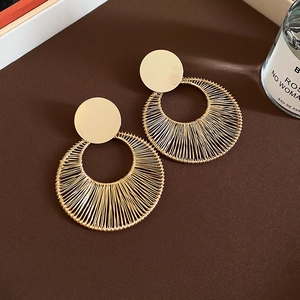 Detail of gold geometric earrings with woven metal ring texture on brown fabric
