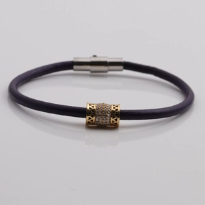 Dettaglio del bracciale in pelle intrecciata viola con ciondoli in zircone dorato e chiusura magnetica