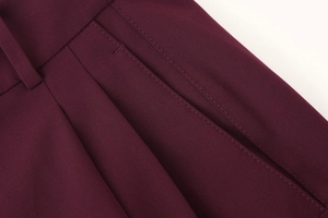 Close-up of deep red bomber suit pants featuring pleated waist and detailed stitching