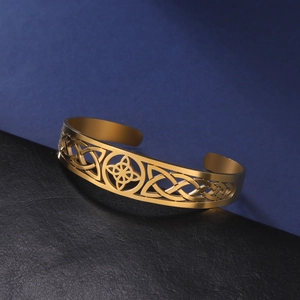 Detail of golden stainless steel open bangle featuring an intricate hollow Celtic knot design