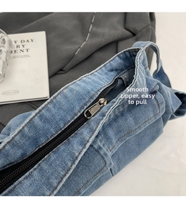 Detail shot of smooth silver zipper and stitching on a blue denim shoulder bag