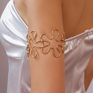 Close-up of golden metal hollow flower arm cuff on model upper arm with silk dress