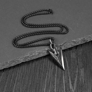 Vintage black metal arrowhead pendant necklace with feather texture on stone background
