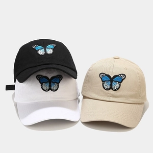 Détail de trois casquettes de baseball en coton noir blanc et kaki avec broderie papillon