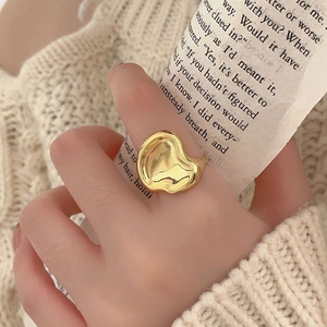 Close-up of a wavy textured golden heart ring worn by a model against a soft knit background