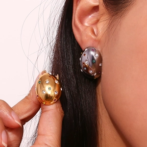 Macro detail of oval gold stud earrings with colorful cubic zirconia on earlobe