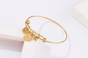 Macro detail of gold Elizabeth II coin and heart pendant on a steel bead bracelet