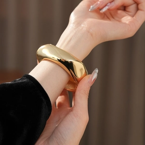 Detail of a wavy gold plated cuff bracelet with a high-polished mirror finish on a model