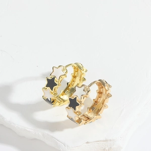 Detailed close-up of golden star hoop earrings with black and white enamel on a white stone