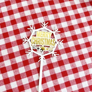 Detailed view of snowflake-shaped Merry Christmas acrylic cake topper on festive fabric