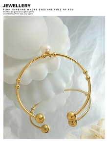 Detailed close-up of a golden open bangle featuring faux pearls and small metal beads