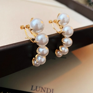 Macro detail of curved pearl earrings with gold-tone base on a premium jewelry box