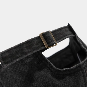 Detail of adjustable bronze metal buckle and washed black fabric on the baseball cap