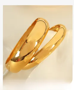 Detail of two high-polish golden titanium steel bangles on a wavy textured surface