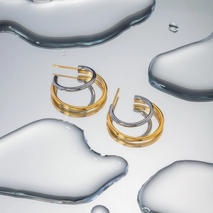 Detailed view of gold and silver two-tone C-hoop earrings on a reflective water surface