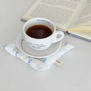Floral ceramic coffee cup and saucer set with a thick bow-patterned padded fabric coaster