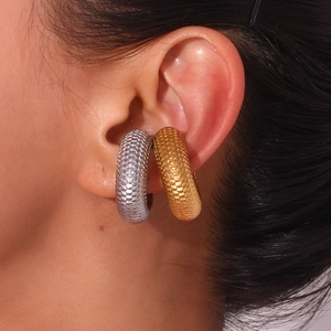 Macro detail of thick 18K gold and silver C-shaped earrings with textured fish scale pattern