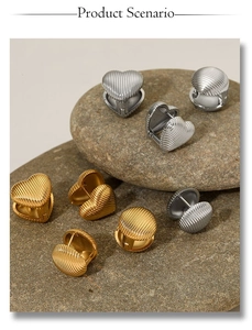 Detail of ribbed heart and circular stud earrings in gold and silver on pebbles