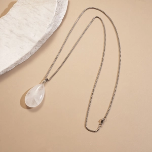 Detailed shot of white teardrop stone pendant with a silver chain on stone background