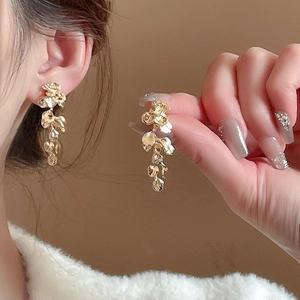 Detailed view of long gold tassel earrings with irregular metallic flower petal charms